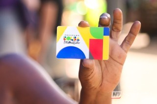 Cartão do programa Bolsa Família em primeiro plano com uma chave de veículo e o vulto de um carro ao fundo, simbolizando a fiscalização de patrimônio.
