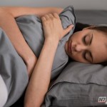 Visão em close de uma porta de madeira fechada em um quarto escuro durante a noite, com foco na maçaneta e na fresta de luz inferior.