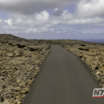 Vista aérea de uma estrada asfaltada reta cruzando um vasto corpo d'água, com margens inundadas em ambos os lados sob um céu claro.