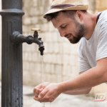 Close em uma torneira externa de metal com pingentes de gelo pendurados, ilustrando o congelamento da água devido ao frio extremo em uma cidade brasileira.