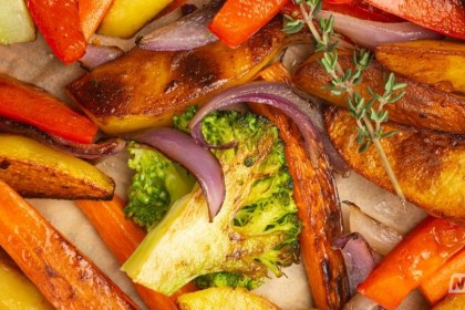 Close-up de legumes variados assados em uma assadeira, exibindo uma camada externa dourada e crocante com interior fumegante.