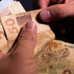 Interface do aplicativo Caixa Tem em um smartphone com foco nos valores de benefícios sociais de abril.