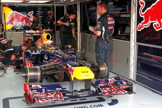 Max Verstappen com expressão séria vestindo o uniforme da Red Bull Racing em um paddock de Fórmula 1.