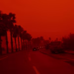 Vista panorâmica de uma cidade coberta por uma densa nuvem de poeira de coloração laranja intensa, com prédios parcialmente ocultos pela névoa.