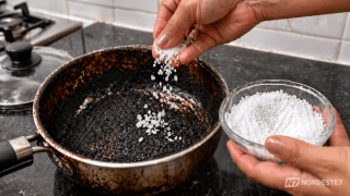 Mão jogando sal grosso sobre o fundo de uma panela de metal com manchas escuras de queimado.