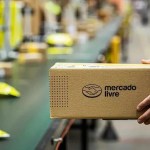 Caixa de papelão aberta com logotipo do Mercado Livre contendo dezenas de currículos impressos em papel branco.