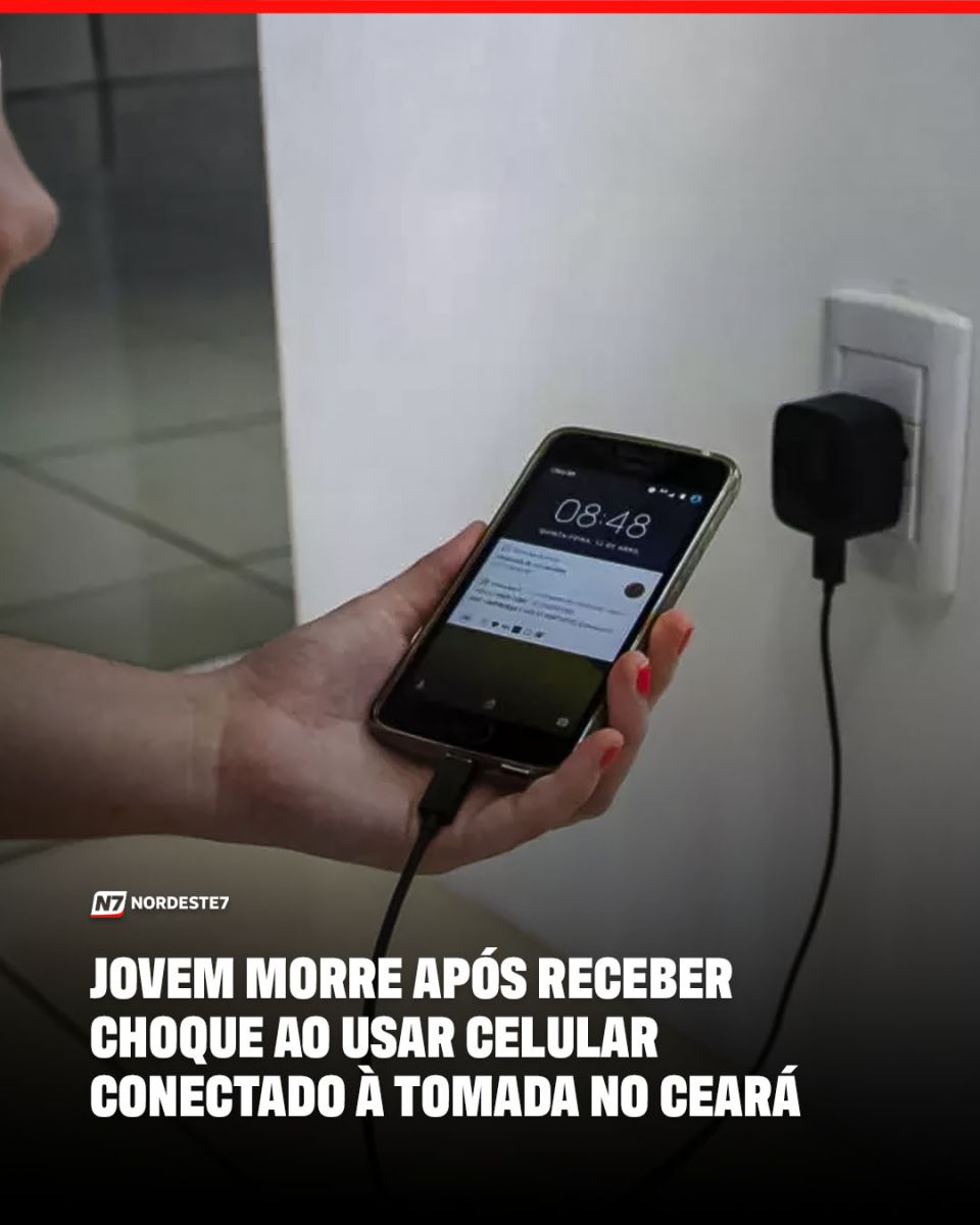 Close-up de um smartphone conectado a um carregador na tomada de parede, ilustrando riscos de choque elétrico.