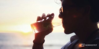 Copo de água com limão e chás naturais dispostos em uma mesa iluminada, simbolizando bebidas matinais para a saúde do fígado.