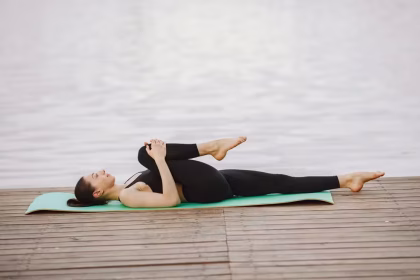 Pessoa deitada sobre um tapete de yoga praticando alongamentos leves em uma sala iluminada.