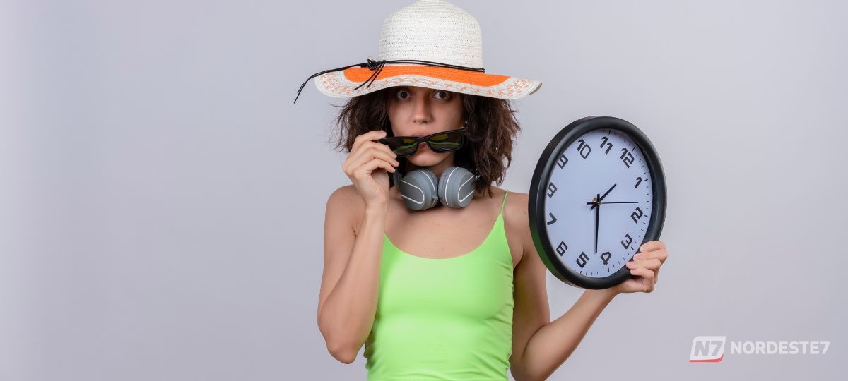 Pessoa ajustando os ponteiros de um relógio de pulso analógico adiantando uma hora, representando a possível volta do horário de verão no Brasil.