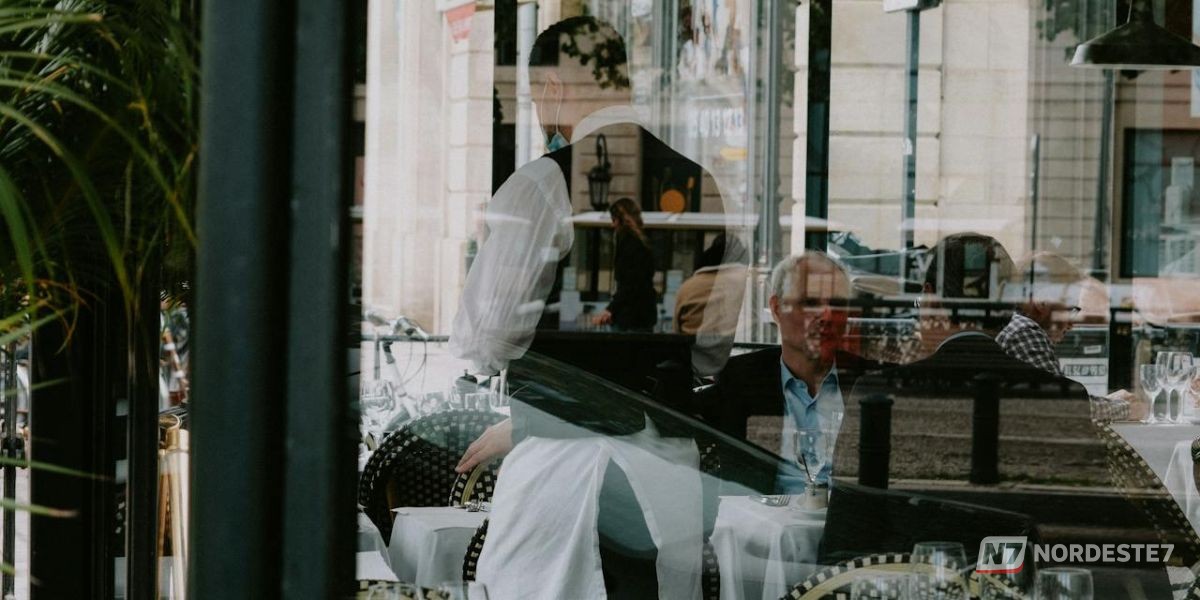 Foto de ângulo médio mostrando a mão de um cliente entregando educadamente um prato empilhado a um garçom em um restaurante, ilustrando o ato de ajudar a recolher a mesa.