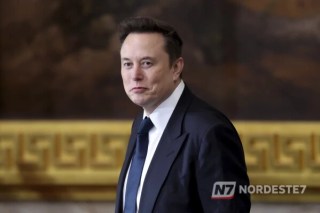 Foto de Elon Musk em primeiro plano com um mapa digital da América do Sul ao fundo, destacando a região de fronteira com o Brasil iluminada por conexões de satélite da Starlink.