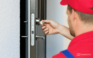 Close-up de um chaveiro profissional trocando uma fechadura de entrada antiga e desgastada em uma porta de madeira, destacando a vulnerabilidade da segurança residencial.