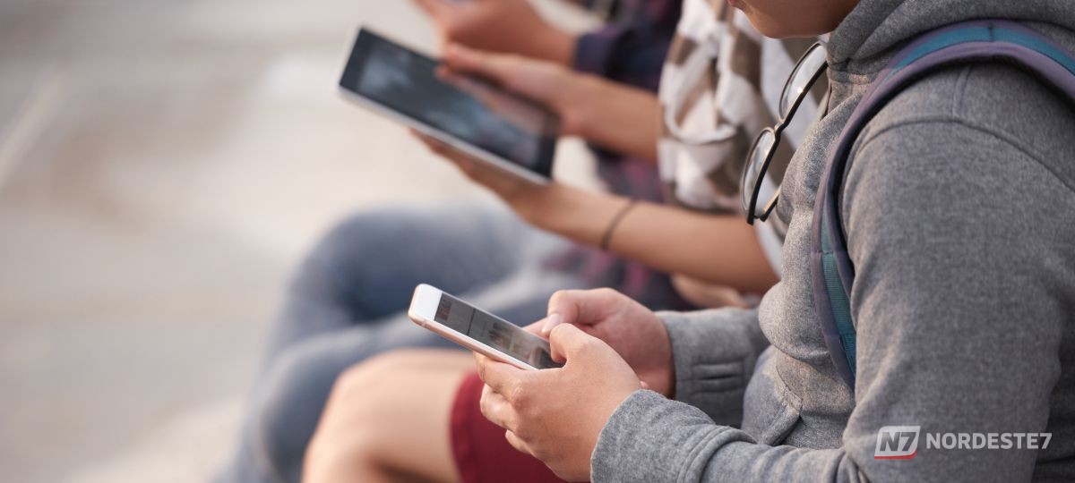 Celular exibindo aplicativo de rede social em primeiro plano desfocado, com uma pessoa ao fundo atrás de grades digitais, ilustrando a relação entre desafios virtuais e detenção.