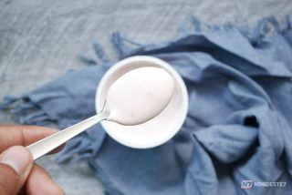 Comparação visual de uma colher com iogurte natural consistente ao lado de um copo com bebida láctea mais fluida em uma mesa de café da manhã, destacando as texturas diferentes.