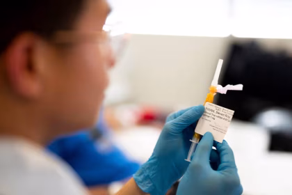 Frasco de vacina sendo preparado por profissional de saúde com luvas em um laboratório clínico na Inglaterra, representando a nova imunoterapia contra o câncer.