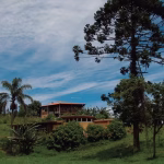 Fachada de uma aconchegante casa de campo cercada por muito verde em um condomínio rural no interior de São Paulo, representando o refúgio de uma consagrada atriz veterana.