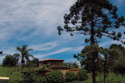Fachada de uma aconchegante casa de campo cercada por muito verde em um condomínio rural no interior de São Paulo, representando o refúgio de uma consagrada atriz veterana.