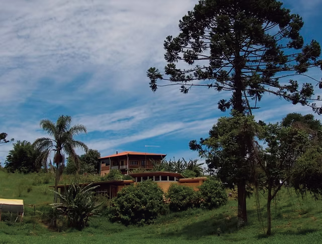Fachada de uma aconchegante casa de campo cercada por muito verde em um condomínio rural no interior de São Paulo, representando o refúgio de uma consagrada atriz veterana.