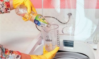 Pessoa despejando uma xícara de produto de limpeza em uma máquina de lavar repleta de roupas brancas.