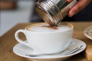 Mão adicionando uma pitada de sal sobre uma xícara de café preto fumegante