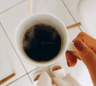 Xícara de café preto puro fumaçando sobre uma mesa de madeira, em iluminação suave.