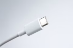 Foto em close-up de um cabo carregador USB Tipo-C sendo conectado a um smartphone sobre uma mesa de trabalho.